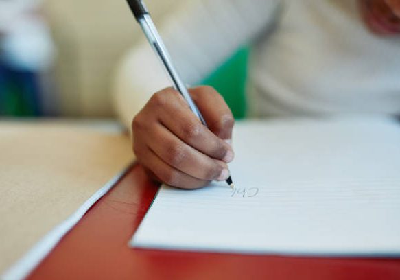 Cropped shot of a young girl writing in a notepad at her classroom desk