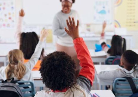 Children, back and hands raised at school with for question, answer and learning at youth academy. Kids, education and teacher for development with sign for talking, quiz and scholarship in classroom