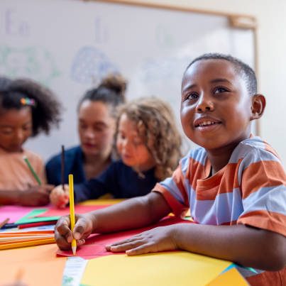 Happy African American schoolboy drawing in class at the kindergarten and smiling - education concepts